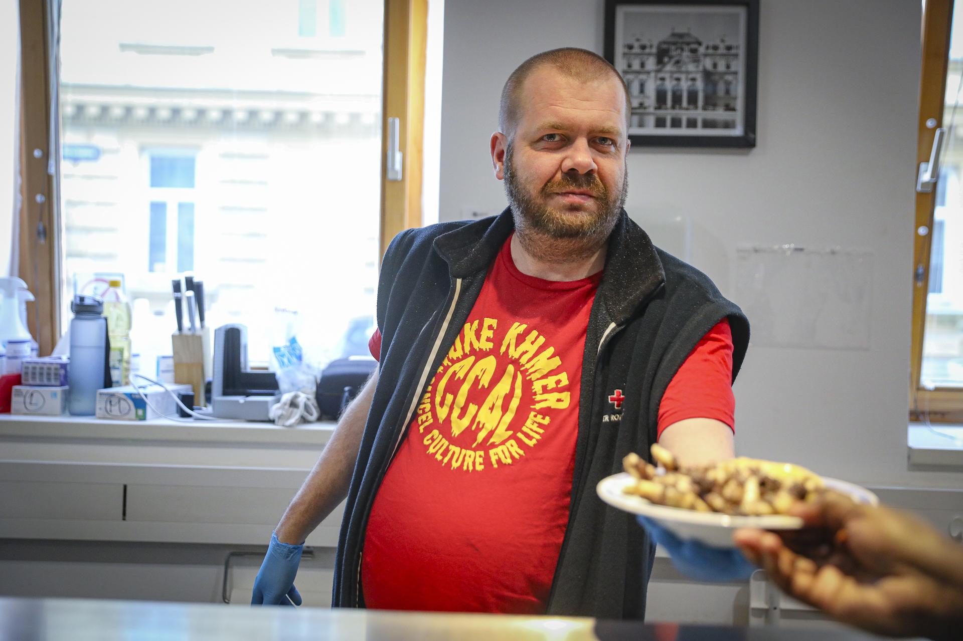 Mitarbeiter der Wohnungslosenhilfe reicht Teller mit warmen Essen einem wohnungslosen Menschen Mitarbeiter der Wohnungslosenhilfe reicht Teller mit warmen Essen einem wohnungslosen Menschen