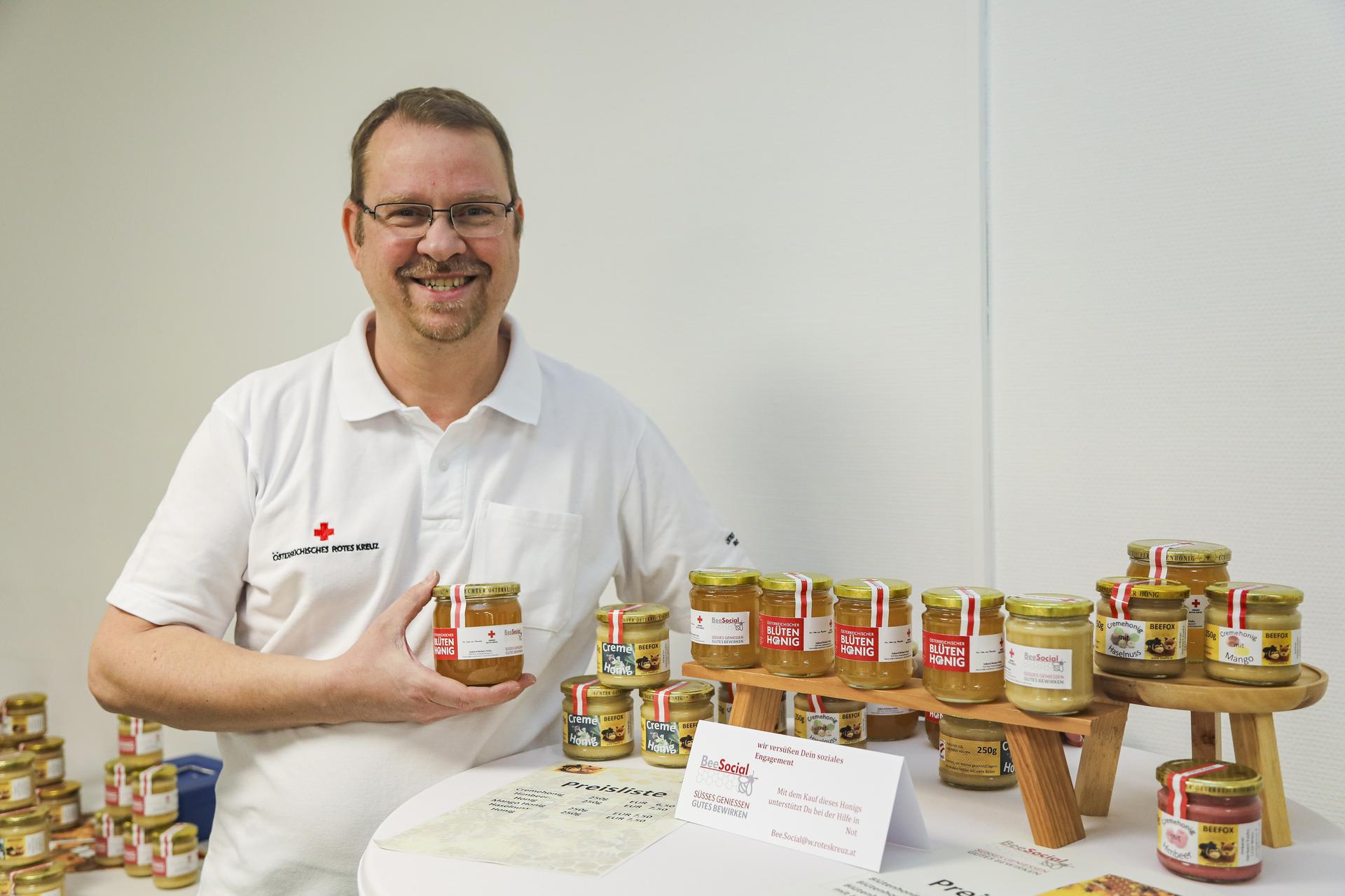 Mann lächelt in die Kamera und präsentiert den Honig des Wiener Roten Kreuzes